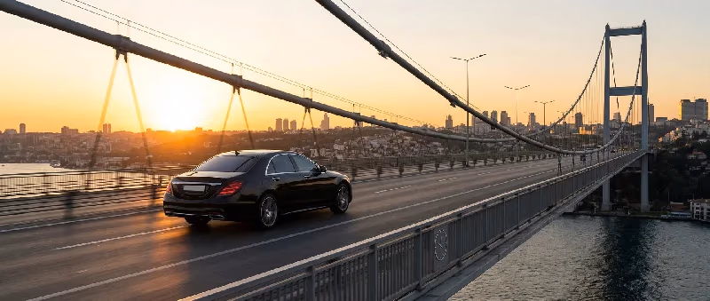 Siyah Mercedes S-Class gün batımında Boğaziçi Köprüsü'nden geçerken arkasında İstanbul silüeti — Elemen Transfer.