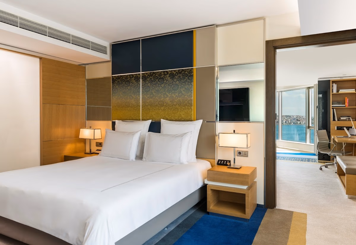 Swissotel suit odası, şık yatak ve şehir manzaralı ofis bölümü.