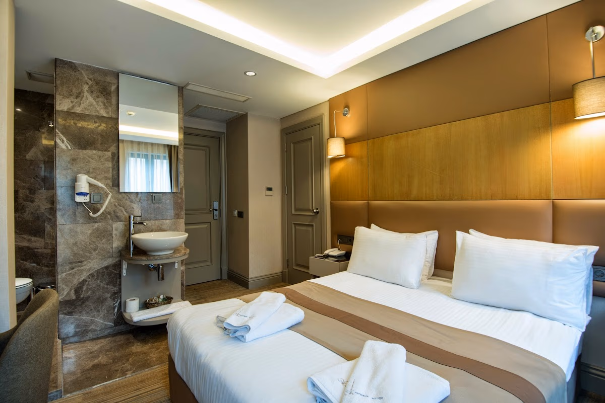 Modern otel odası, çift kişilik yatak ve mermer banyo detayları.
