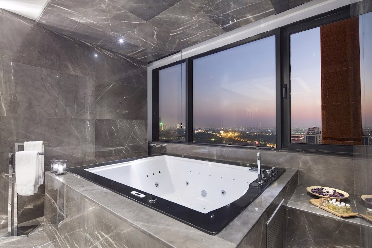 Luxurious marble bathroom in a Hilton Istanbul Maslak suite with a jacuzzi tub overlooking the city lights at night.