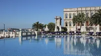 Beskrajni bazen palače Çırağan Kempinski s pogledom na Bospor po sunčanom danu, s povijesnom zgradom palače.