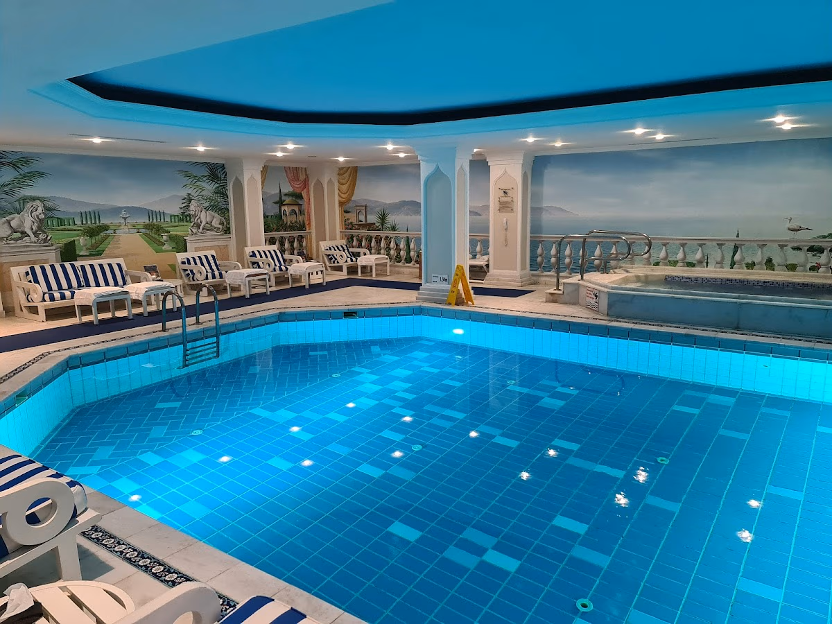 Serene indoor swimming pool at Çırağan Palace Kempinski, with blue ambient lighting, classical columns, and wall murals.