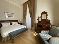 Klasična soba hotela Pera Palace s drvenim krevetom, plavom klupom, antiknim toaletnim stolićem i velikim prozorom sa zlatnim zavjesama.