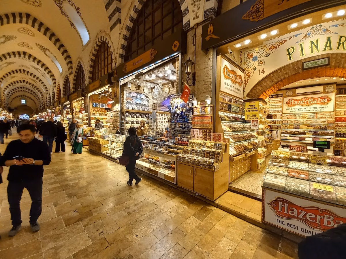 People walking through the historic vaulted corridors of the Spice Bazaar with shop displays.