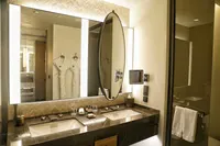 Luxury bathroom interior with double vanity, marble countertop, illuminated mirrors, and white bathrobes