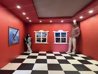 Two people posing in an Ames room optical illusion at Vialand Theme Park.