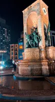 Illuminated Taksim Republic Monument statues and city buildings at night.