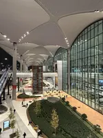 High-angle view of Istanbul Airport's vast, multi-level terminal at night, with indoor gardens and a large glass facade.