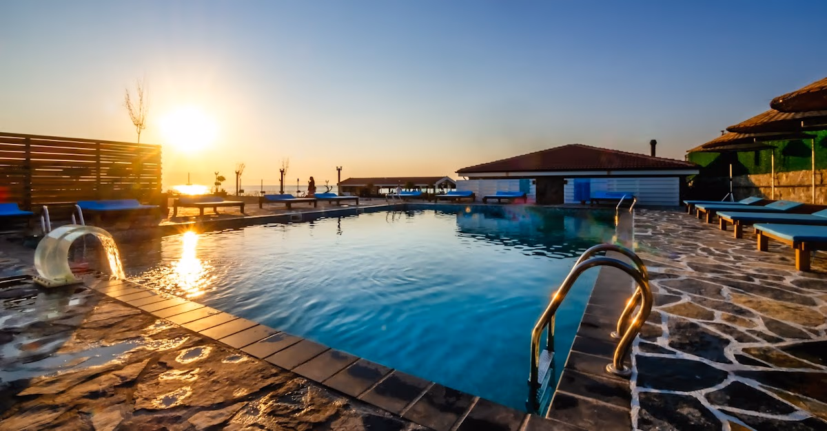Marin Beach Hotel'in yüzme havuzunda gün batımı, şezlonglar ve arka planda deniz manzarası.