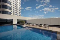 İstanbul Marriott Hotel Pendik'in modern binası ve mavi gökyüzü manzaralı, şezlonglu çatı katı havuzu.