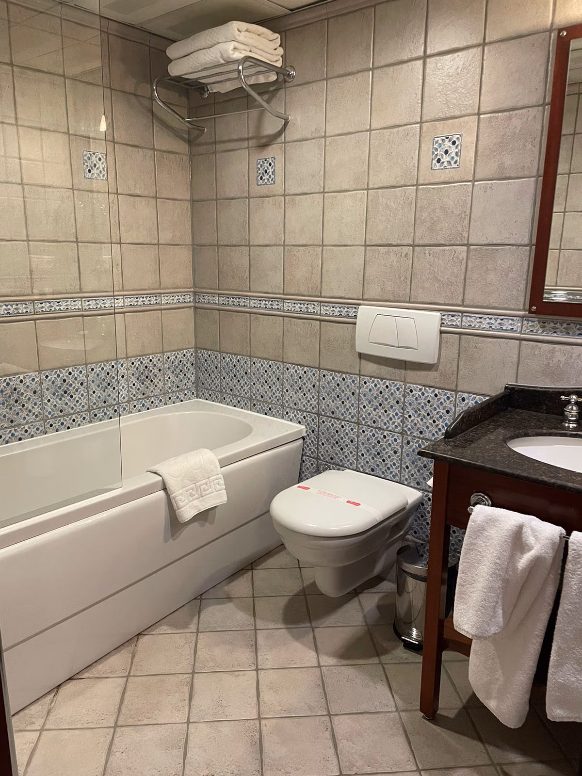 O baie curată și modernă la Sirkeci Mansion, dotată cu o cadă, gresie elegantă și un mobilier de baie din lemn închis la culoare.