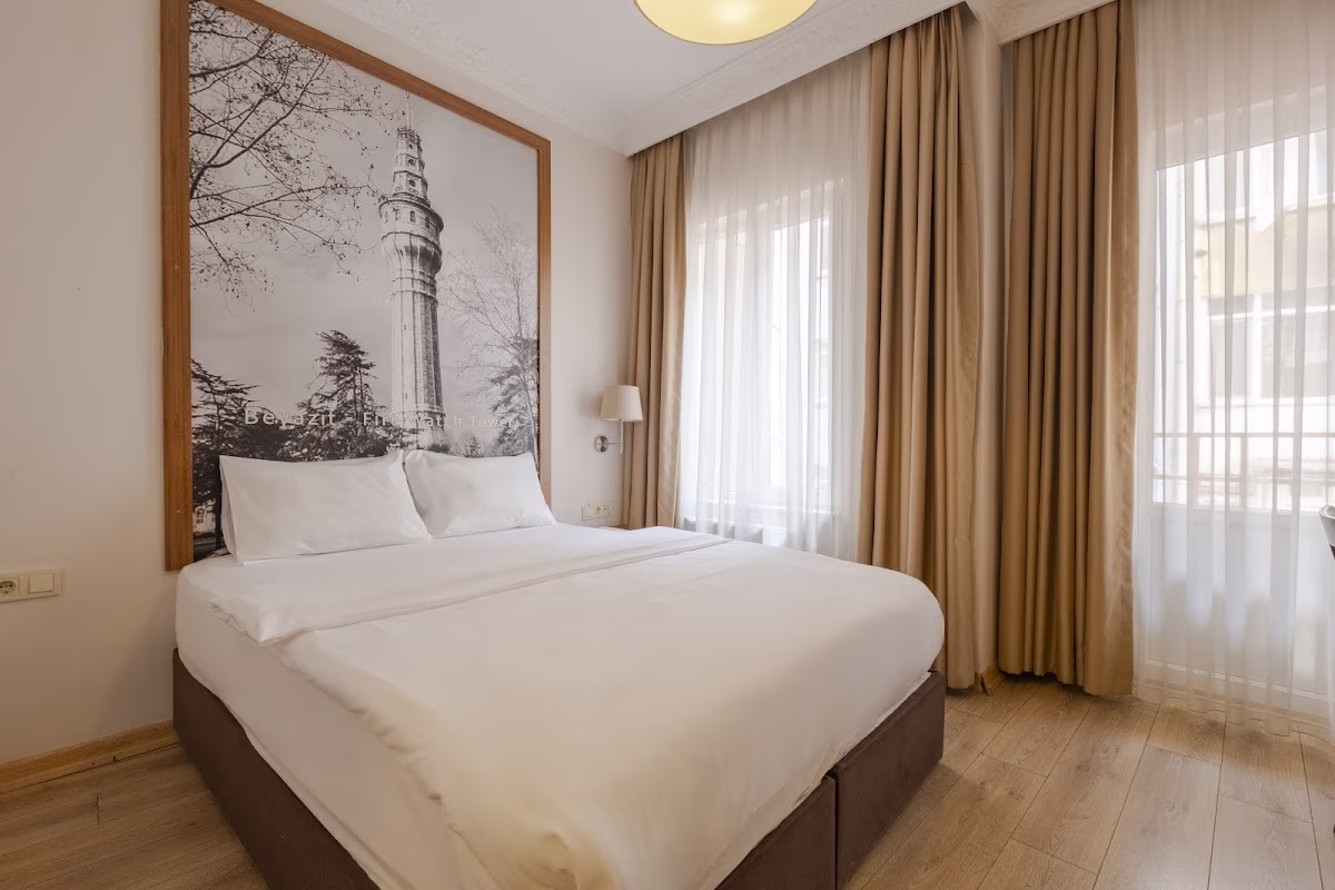 A comfortable double bed with white linens in a brightly lit room at MLS Şişli Hotel, with a large tower artwork on the wall.