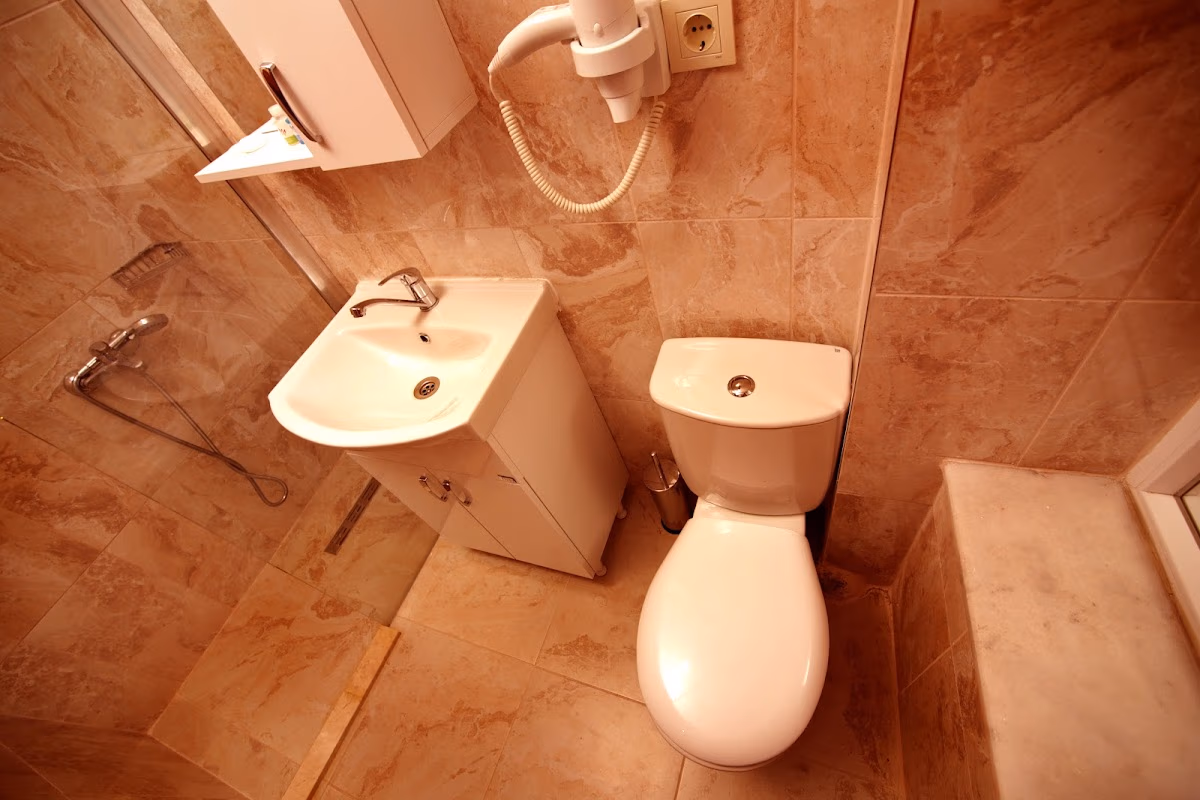 A clean, compact bathroom at MLS Şişli Hotel with marble-patterned tiles, a modern sink, toilet, and shower area.