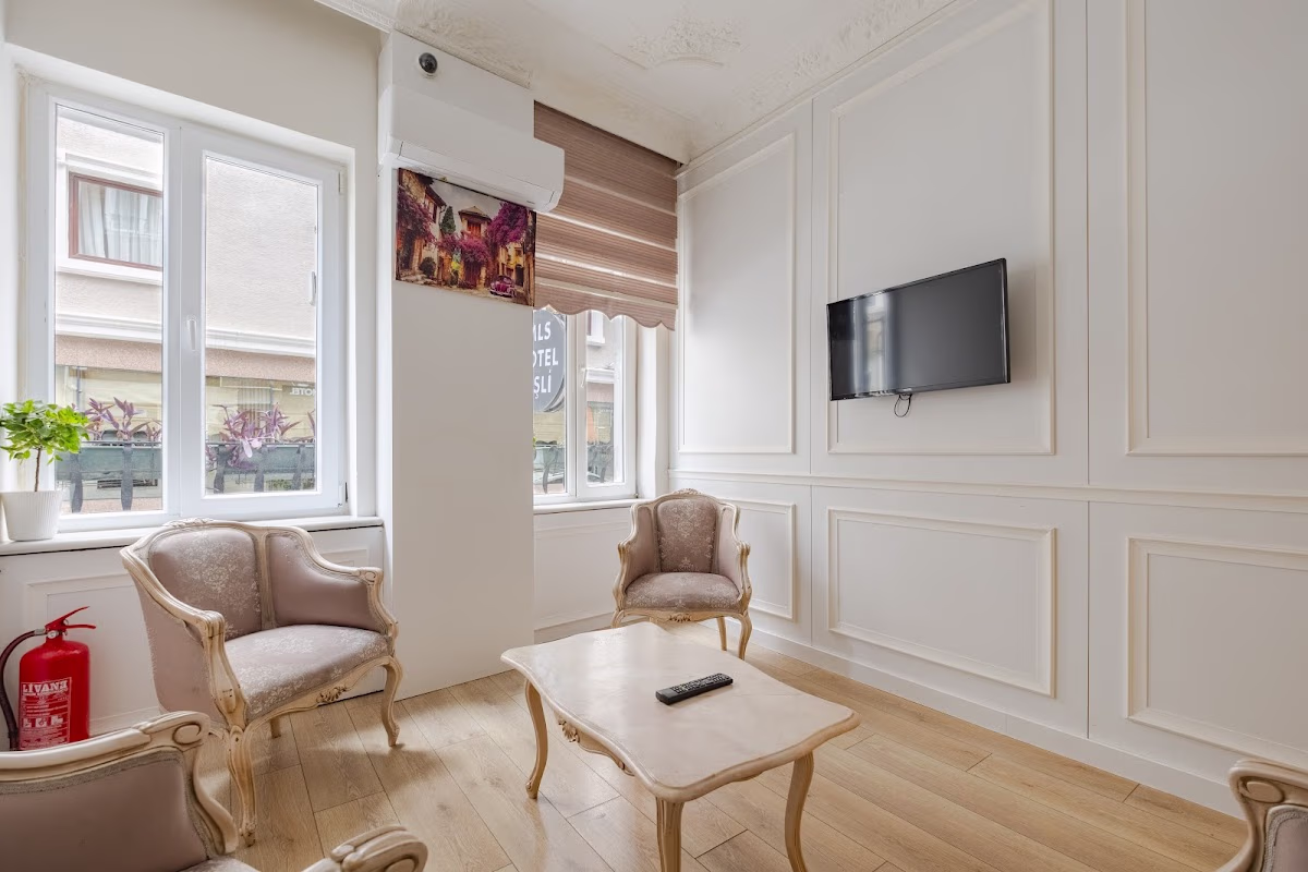 The elegant lobby lounge at MLS Şişli Hotel, featuring classic armchairs, a coffee table, and a TV on a white paneled wall.