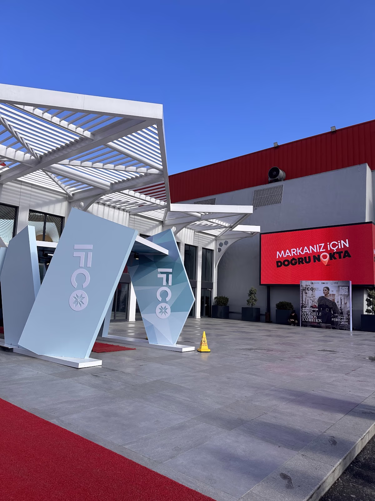 IFCO giriş alanı, modern geometrik yapılar ve kırmızı halı üzerinde dijital reklam ekranı.