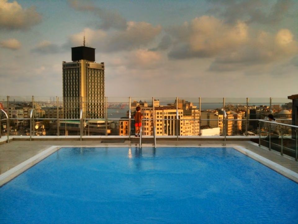 Taksim Gönen Otel'in çatı katı havuzu ve merdiveninde duran bir kişi, arkada İstanbul şehir manzarası.