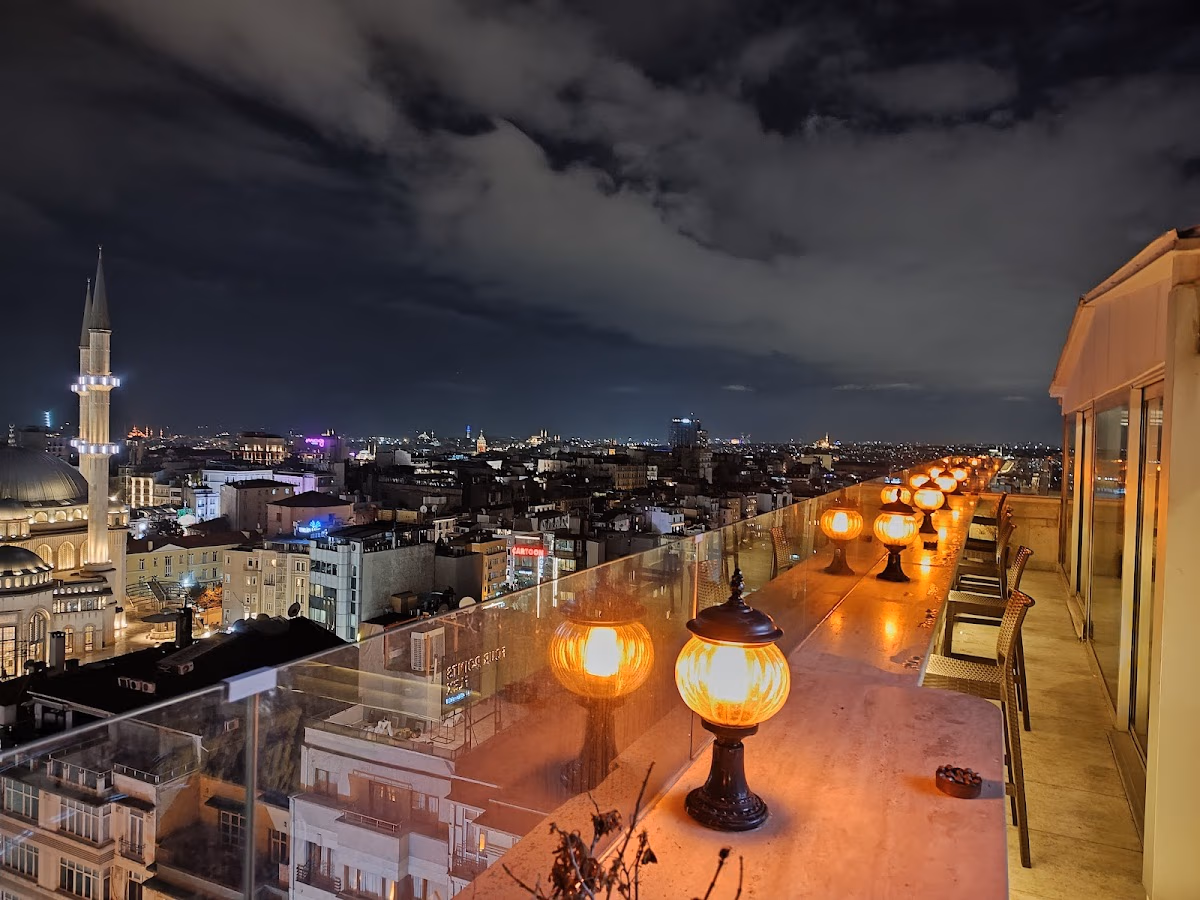 Taksim Gönen Otel'in çatı terasından aydınlatılmış cami ve şehir ışıklarının gece manzarası.