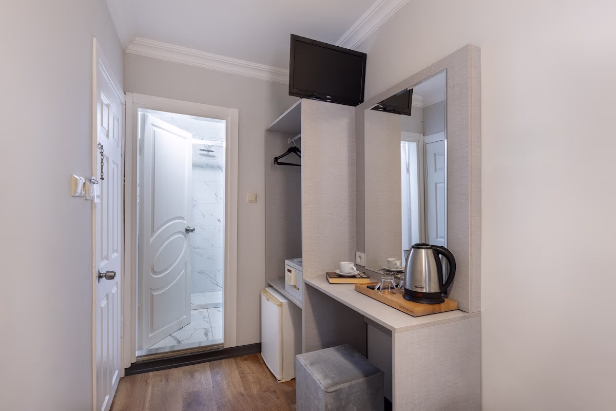 Taksim Trust Hotel odasında makyaj masası, ayna, mini buzdolabı ve banyo manzarası sunan iyi donanımlı bir köşe.