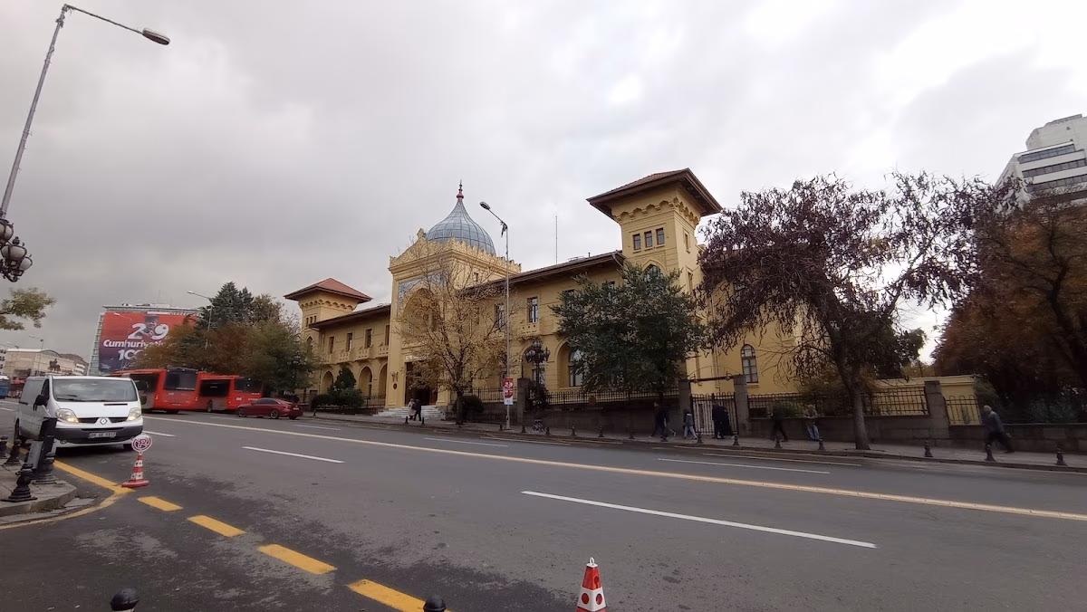 The historic Ankara Palas building viewed from across the street, showcasing its grand facade, dome, and towers on a cloudy day.