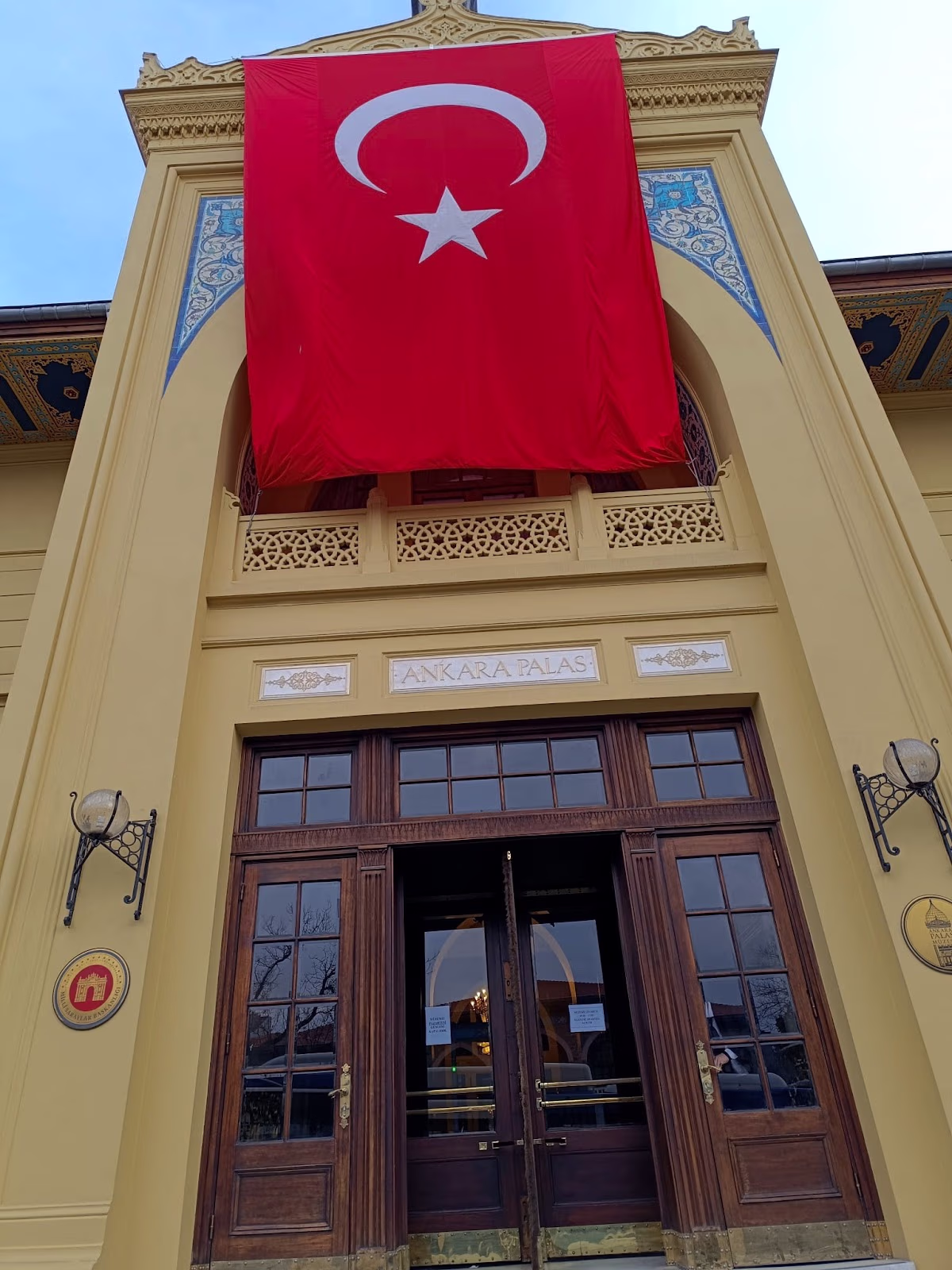 Close-up of the main entrance of Ankara Palas, with a large Turkish flag hanging above the ornate wooden doors.