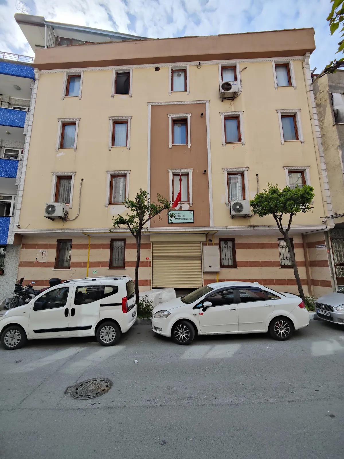 The beige facade of Bağcılar Özel Songül Alkan Kız Öğrenci Yurdu, a four-story building with cars parked on the street in front.