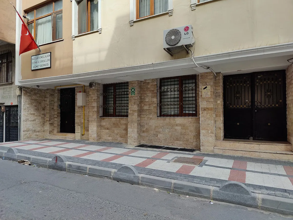 Ground-level view of the stone-clad entrance to a building in Bağcılar, with barred windows and a patterned sidewalk.