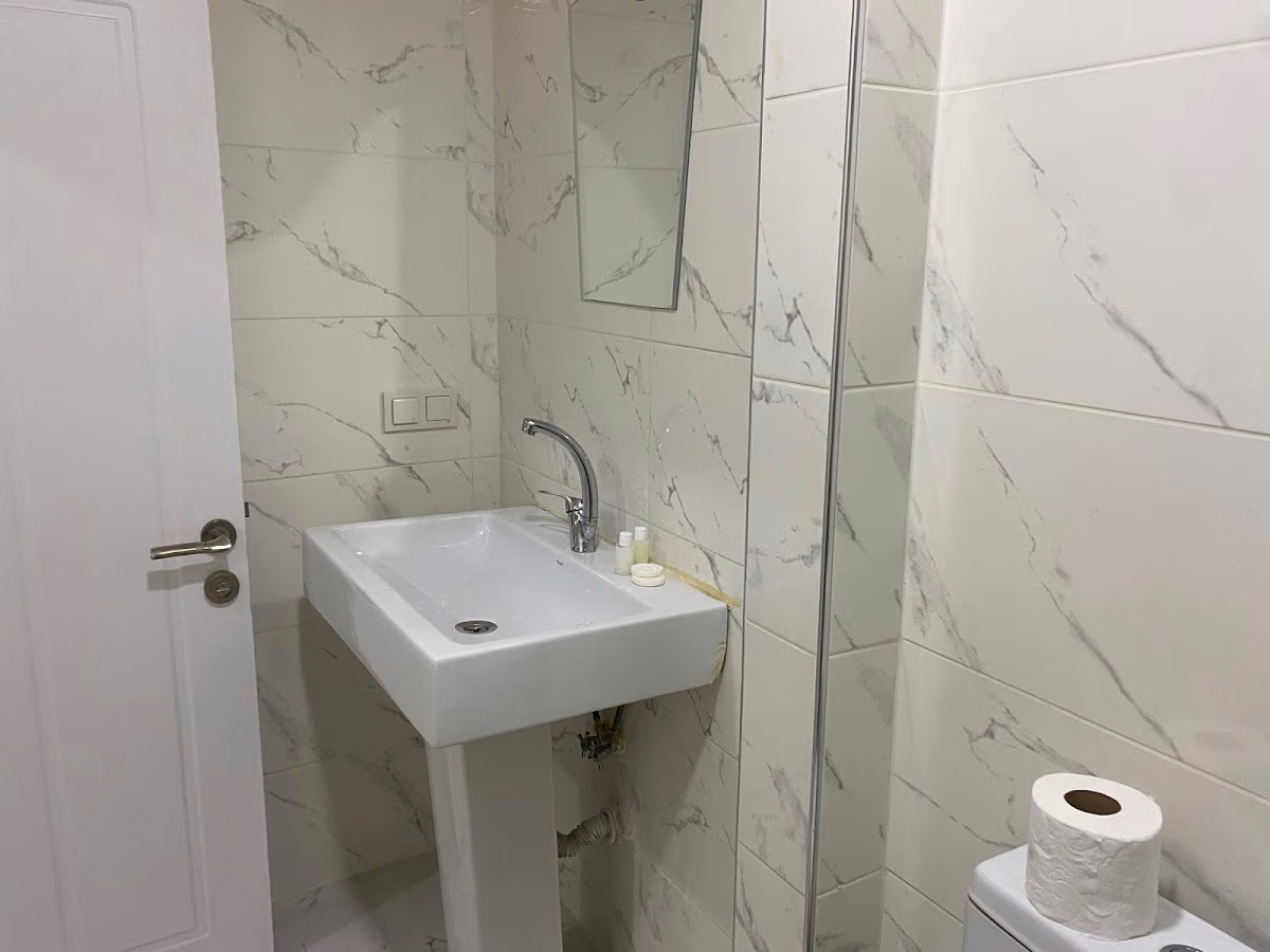 The modern and clean bathroom at Bağcılar Kümbet Otel, featuring white marble-patterned tiles.