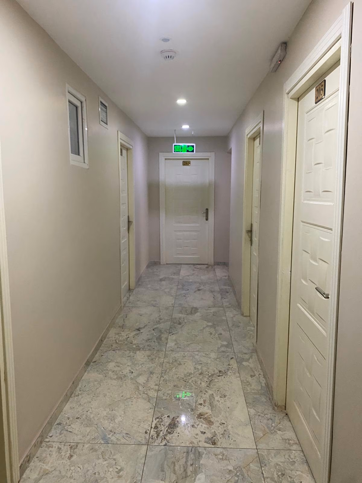 The quiet, well-lit corridor of Bağcılar Kümbet Otel with marble floors and guest room doors.